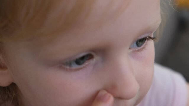 A little girl chews a candy and fixes her snotty nose