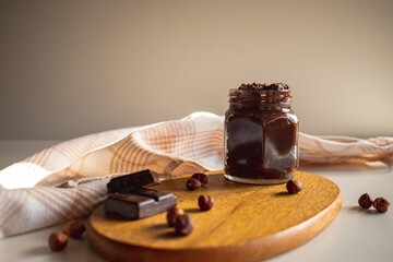Table with a jar of homemade vegan hazelnut cream, with hazelnuts scattered around and chocolate bars used in the recipe