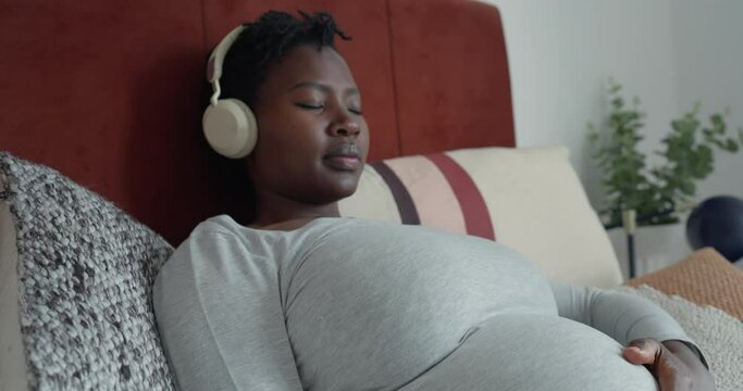 Pregnant woman listening to music while resting on bed