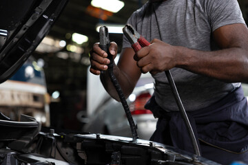 close up mechanic worker hands holding battery cable for jumping battery of a car in automobile repair shop
