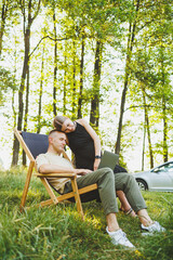 Fototapeta premium A happy man and his pregnant wife are working on a laptop while sitting in nature. A young couple is relaxing in nature and watching a movie on a laptop.