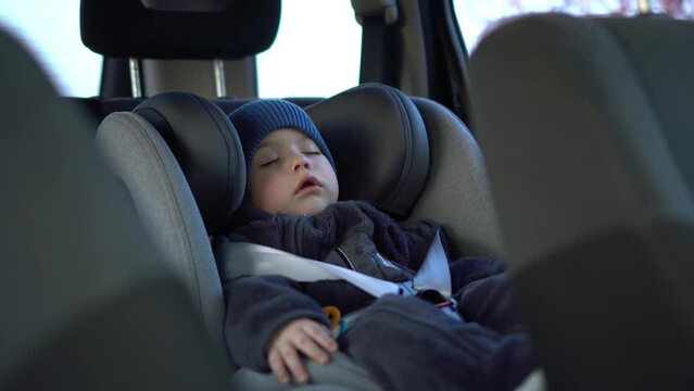 A small child sleeps in a car seat in a parking 