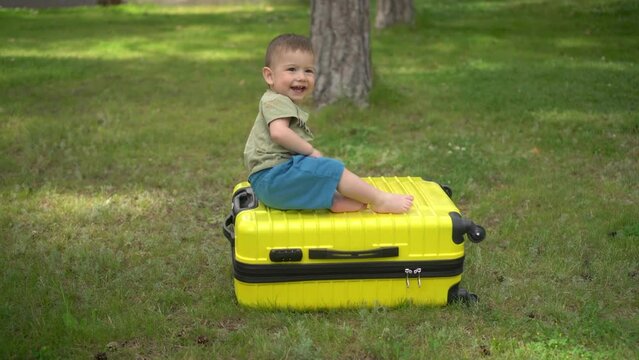 A little boy climbs on a yellow suitcase in nature