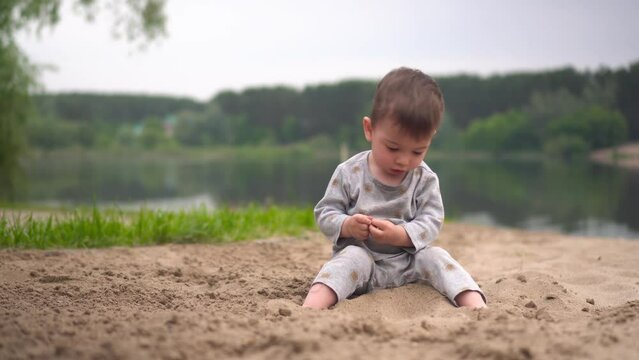 A little boy sits on the beach by the river 