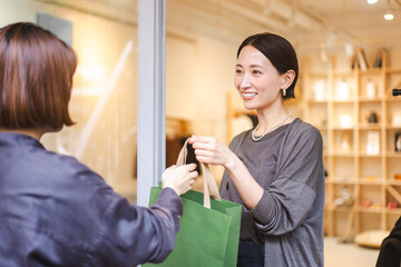働く日本人女性/アパレル店員/お買い上げ商品をお客様に手渡している