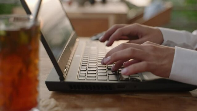 Female dev typing on laptop keyboard in tropical cafe. Software developer writes program code on computer screen in coworking restaurant with sea view on sunset. Woman coding close-up slow motion.