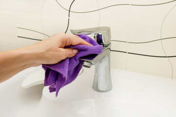 a woman's hand washes a faucet with a rag in the bathroom