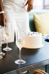 Bachelorette party. Themed cake and champagne glasses on the table with blurred person in the background. Vertical photo. Close up