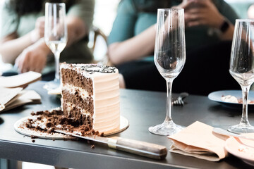 Bachelorette party. Sliced ​​chocolate themed cake and glasses of champagne on the table with blurred people in the background. Horizontal photo. Close up