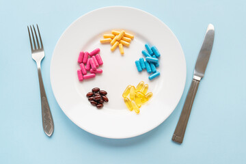 The concept of healthcare, healthy eating, diet. Many multi-colored bright vitamins lie on a plate along with a knife and fork.