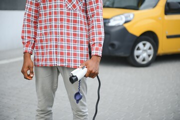 african man holding charge cable in on hand standing near luxury electric car