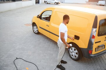 African american Man stands next to electric delivery vans at electric vehicle charging station