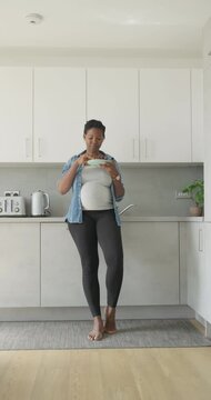 Pregnant woman eating red grapes in kitchen