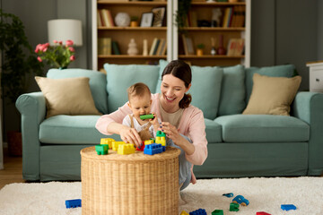 Mother and her baby boy playing with colored toy blocks at home