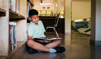 At the library, a young boy of Asian descent is deeply engrossed in reading a book during his break.