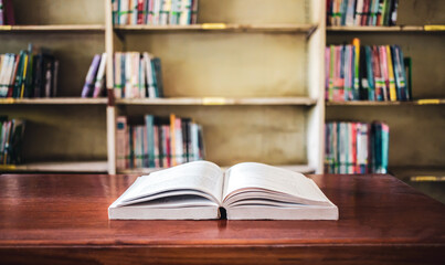 On a wooden table, there's an open book with a library visible in the background. A stack of books nearby adds to the theme of educational learning.