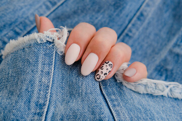 Beautiful female hands with manicure on the background of denim. Stylish nail design. Autumn manicure with beige color and leopard pattern on the nails.