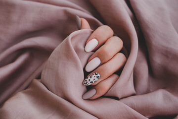 Woman's hand with a beautiful oval-shaped manicure. Autumn trend, beige color polishing with leopard pattern on nails with gel polish, shellac. - obrazy, fototapety, plakaty