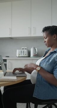 Pregnant woman working on laptop in kitchen