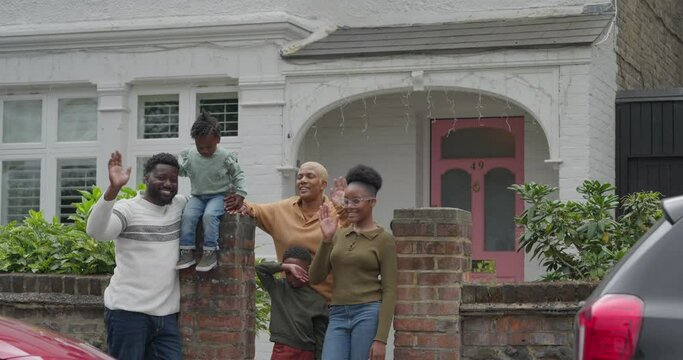 Portrait of smiling family standing in front of house and waving to camera