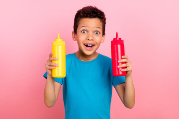 Photo portrait of сute little boy hold excited mustard ketchup bottles wear trendy blue clothes isolated on pink color background