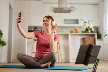 Young woman using smart phone and taking Selfie while exercising yoga at home