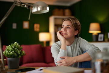 Mid adult woman looking in distance, working on digital tablet at home office