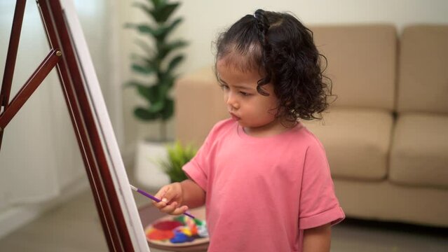 
Happy moment little cute girl creating and water color painting activity with paint brushes on frame canvas at living room. Kids activity. Child physical, Emotional, Cognitive development concept.