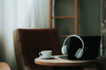 Workplace concept, laptop, headphones and coffee cup on wooden table in house independent home office