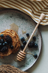 Apetyczne pancake's z domowego przepisu na rustykalnej ceramice z owocami leśnymi i naturalnym miodem. Zmysłowe śniadanie w harmonii natury.