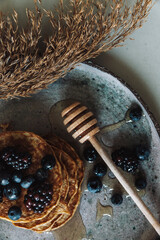 Domowe pancake's na rustykalnej ceramice z owocami leśnymi i naturalnym miodem. Zmysłowe śniadanie w harmonii natury.