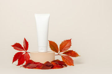 Mockup facial cream bottle on podium with autumn leaves, copy space for design. Seasonal skin care, face cream white tube