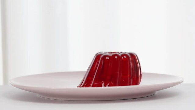 Red homemade jelly falls out of a plastic mold onto a plate, and it quivers on a white background.