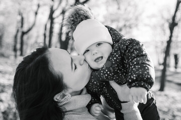 Mom hugging, kissing daughter walk on leaves in forest. Mother throws up child in park. Family spending time together at sunset on vacation. Upper half. Autumn holiday. Closeup. Black and white photo
