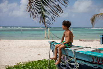 Beautiful little boy sitting on a wooden boat on the beach