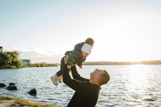 Father throws up child, flying into sky near lake in nature. Family spending time together at sunset on vacation. Dad holds daughter walking in park. Upper half. Concept of autumn holiday. Closeup