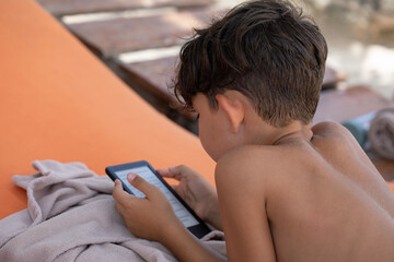 Beautiful little boy reading a kindle on the beach