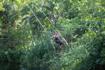 Beautiful young woman on a swing in the jungle