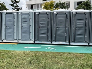 A row of portable toilets outdoors by a bicycle road in a park.