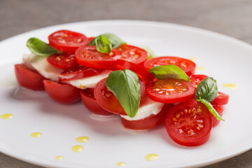 Caprese salad with tomato, mozzarella, basil, olive oil on white plate close up. Mediterranean cuisine. Focusing on the basil leaves. Macro with shallow dof.