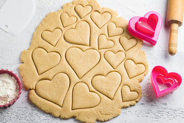 Cutting heart shaped cookies with cookie cutters on a light blue tabletop, top view. Stage of cooking delicious homemade pastry