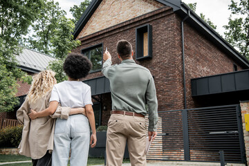 back view of real estate broker showing new cottage to interracial lesbian couple outdoors