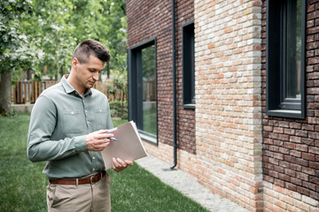 real estate agent holding folder and pen while standing near contemporary building on city street