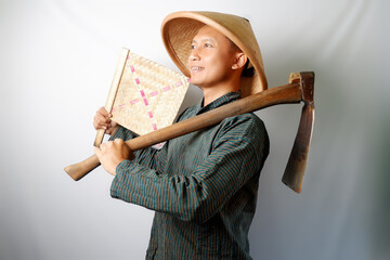 Happy Asian farmer wearing Lurik and Caping looking at camera. His right hand holding a bamboo fan and left hand holding a Cangkul isolated on white background. Human gestures concept