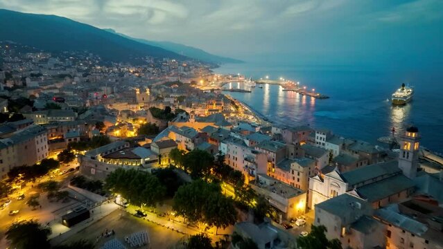 Aerial view of Bastia harbor and old town, ferry leaves the port, mediterranean sea, Corsica, France. Flying over evening Bastia with city lights, Corsica island