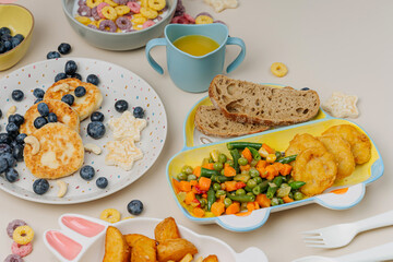 Cute plates with a variety of children's food. Vegetables, nuggets, french fries, pancakes, cereal and juice. Creative serving for baby.  Concept of kids menu, nutrition and feeding.