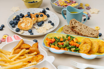 Cute plates with a variety of children's food. Vegetables, nuggets, french fries, pancakes, cereal and juice. Creative serving for baby.  Concept of kids menu, nutrition and feeding.