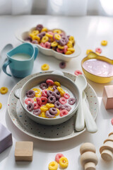 Dry children's breakfast. Cute children's plates and bowl with colorful cereal rings of milk. Creative serving for baby. Mess on the dining table. Concept of kids menu, nutrition and feeding.