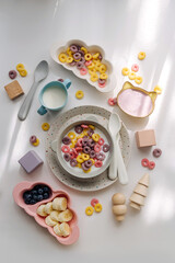 Dry children's breakfast. Cute children's plates and bowl with colorful cereal rings of milk. Creative serving for baby. Mess on the dining table. Concept of kids menu, nutrition and feeding.