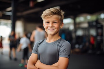 Portrait of smiling boy standing with arms crossed in fitness center.